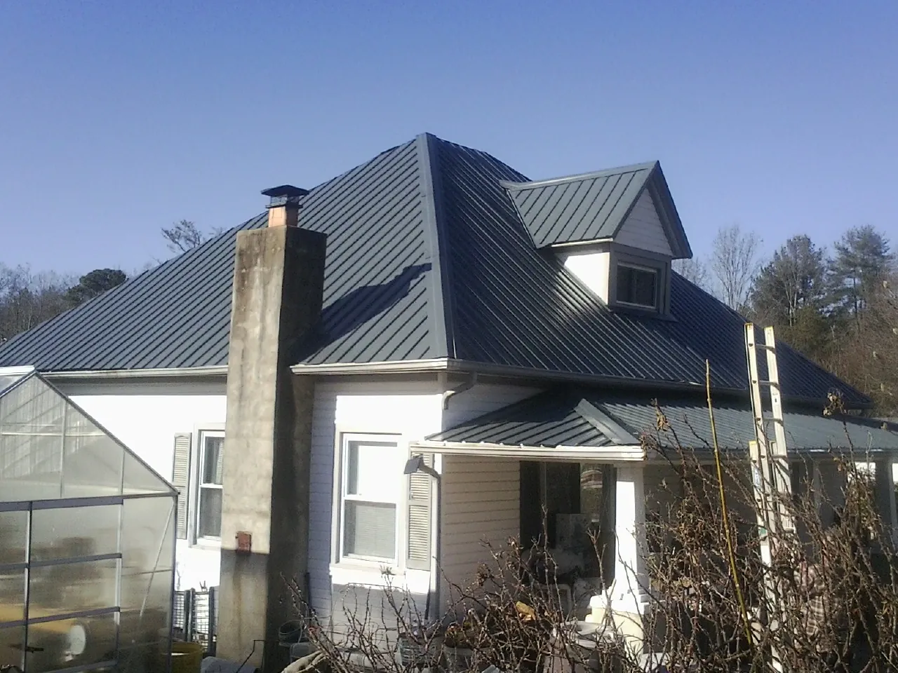 Dark blue standing seam metal roof on a white farmhouse with dormer — Slate & Tile Roof Repair by Roofing Brothers in Urbandale