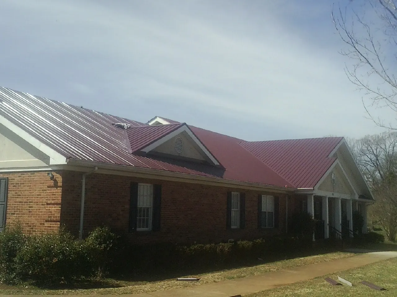 Red metal roof with gabled entries on a long brick building, from a Hail Damage Roof Repair job in Urbandale