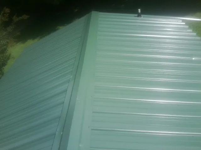 New green metal panels meeting at the ridge of a roof — Flat Roof Repair work by our crew in Urbandale