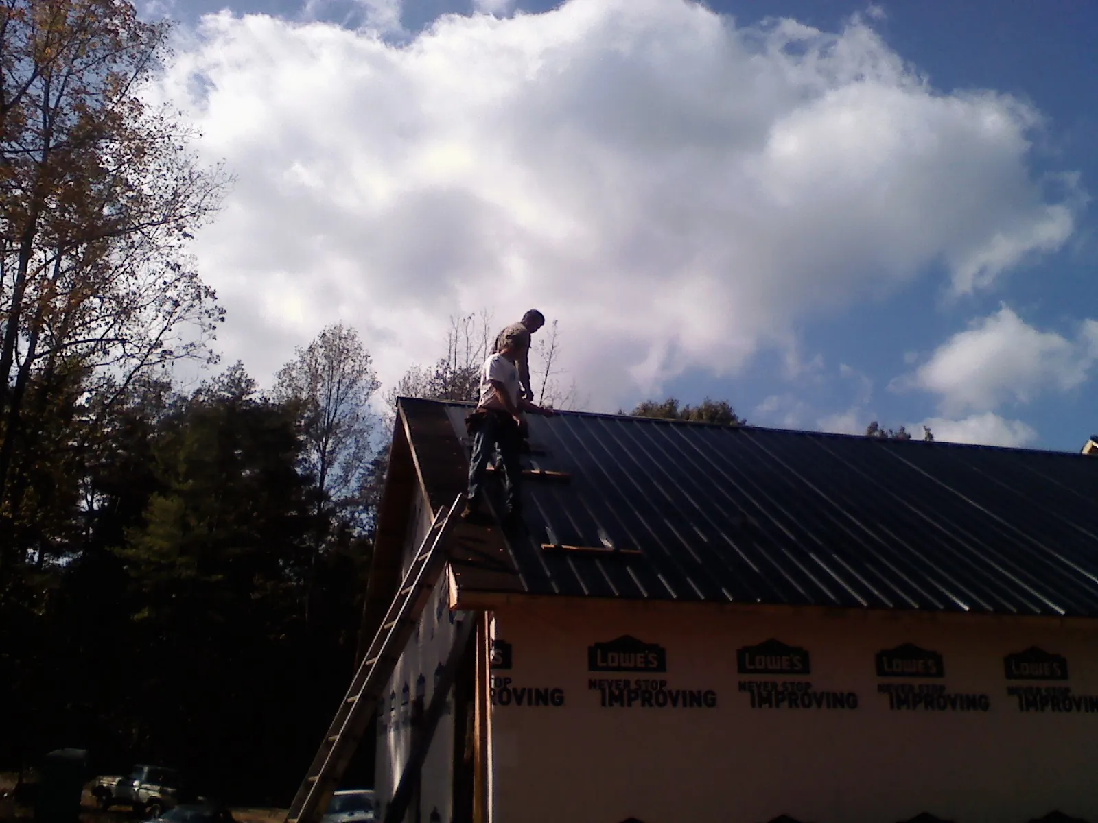 Roofer fastening dark metal panels high against a cloudy sky, from a Roof Inspection job in Urbandale