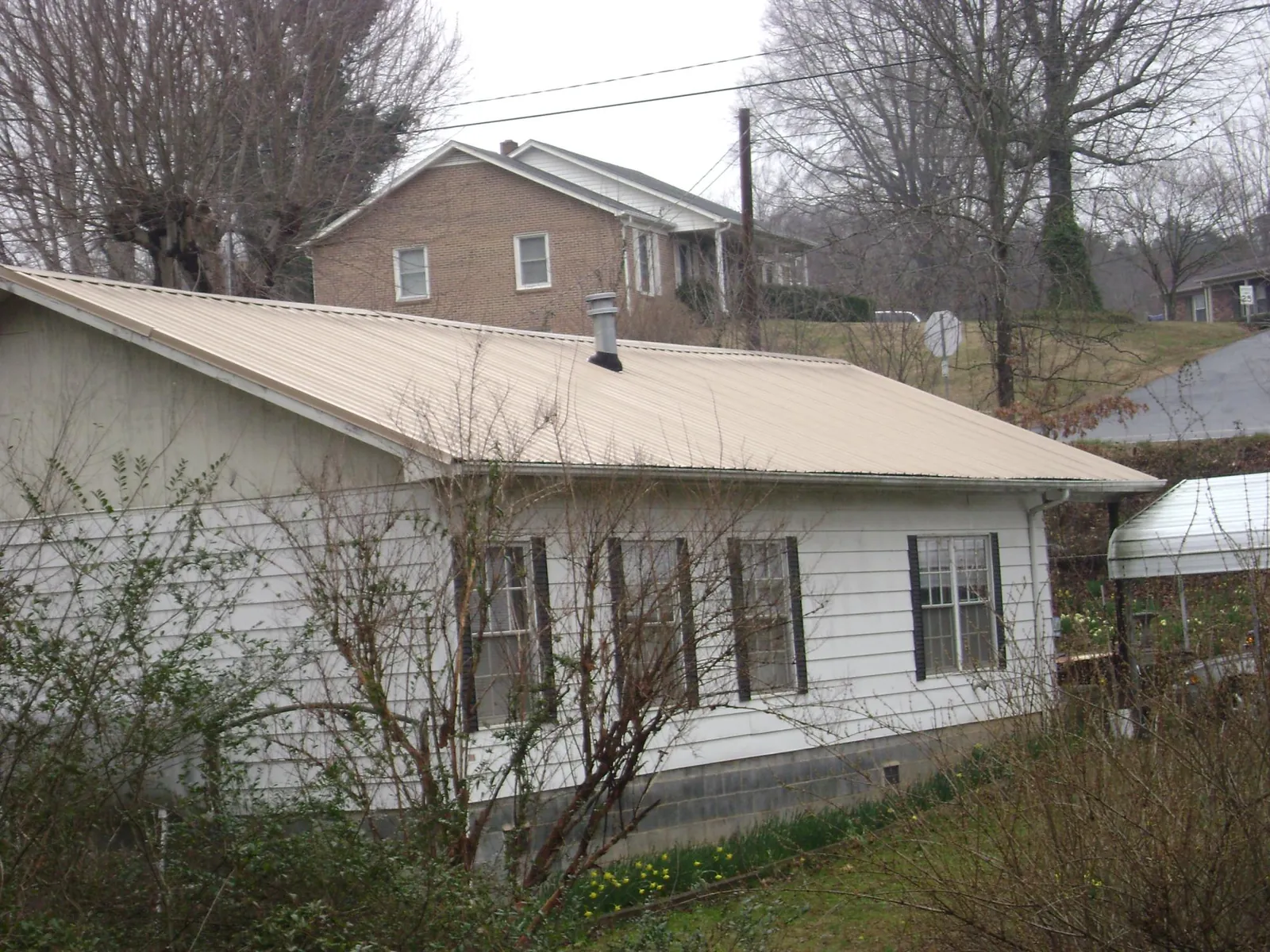 Tan metal roof on a white sided house set into a hillside — Commercial Roofing by Roofing Brothers in Urbandale