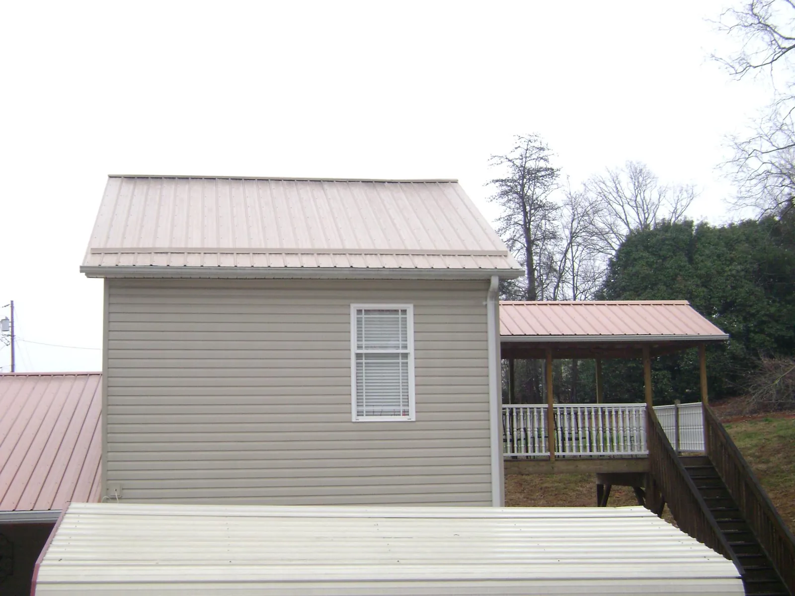 Tan metal roofs on a two story addition and attached porch, from a Roof Replacement job in Urbandale