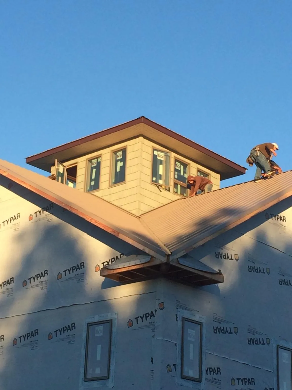 Roofers working around a rooftop cupola on a new metal roof at sunset — Roof Waterproofing in Urbandale by Roofing Brothers